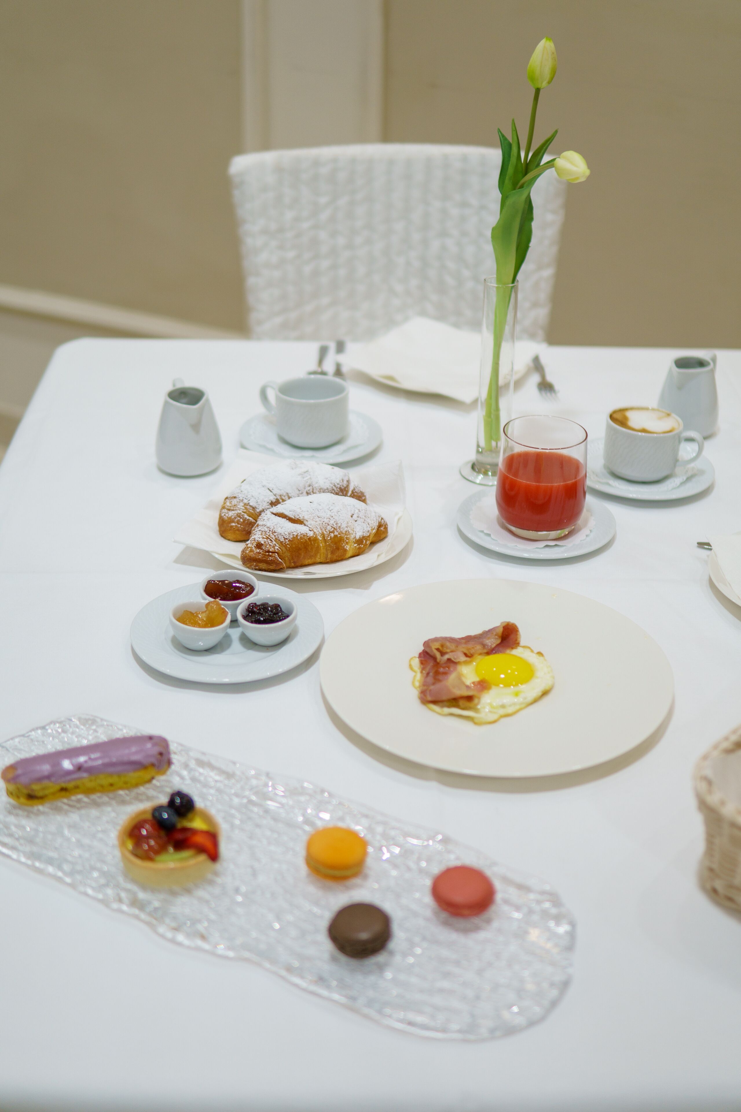 A breakfast table with pastries, a glass of juice, and a vase with flowers.