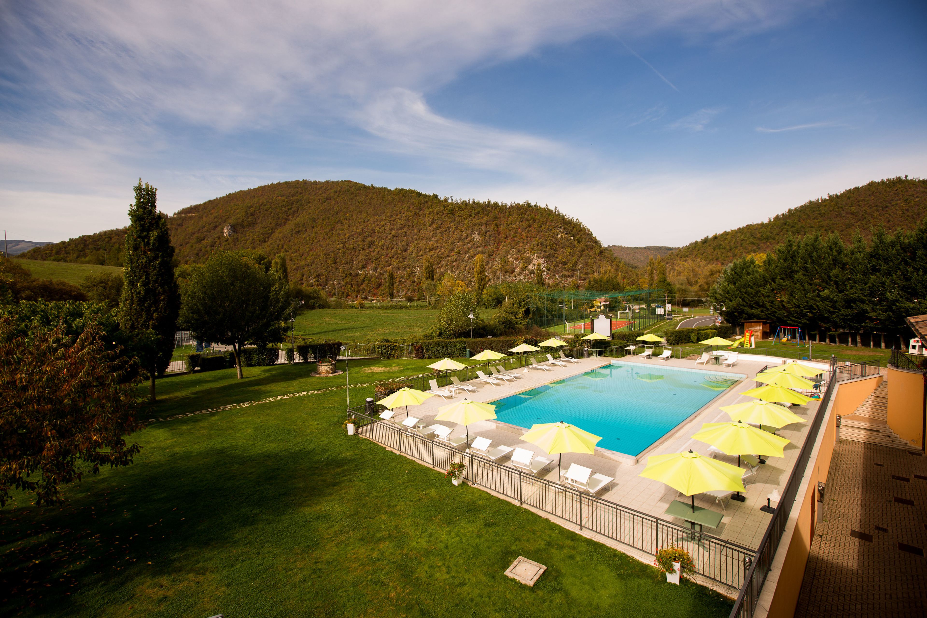 A swimming pool with sun loungers and umbrellas, surrounded by a well-maintained lawn and hills in the background.