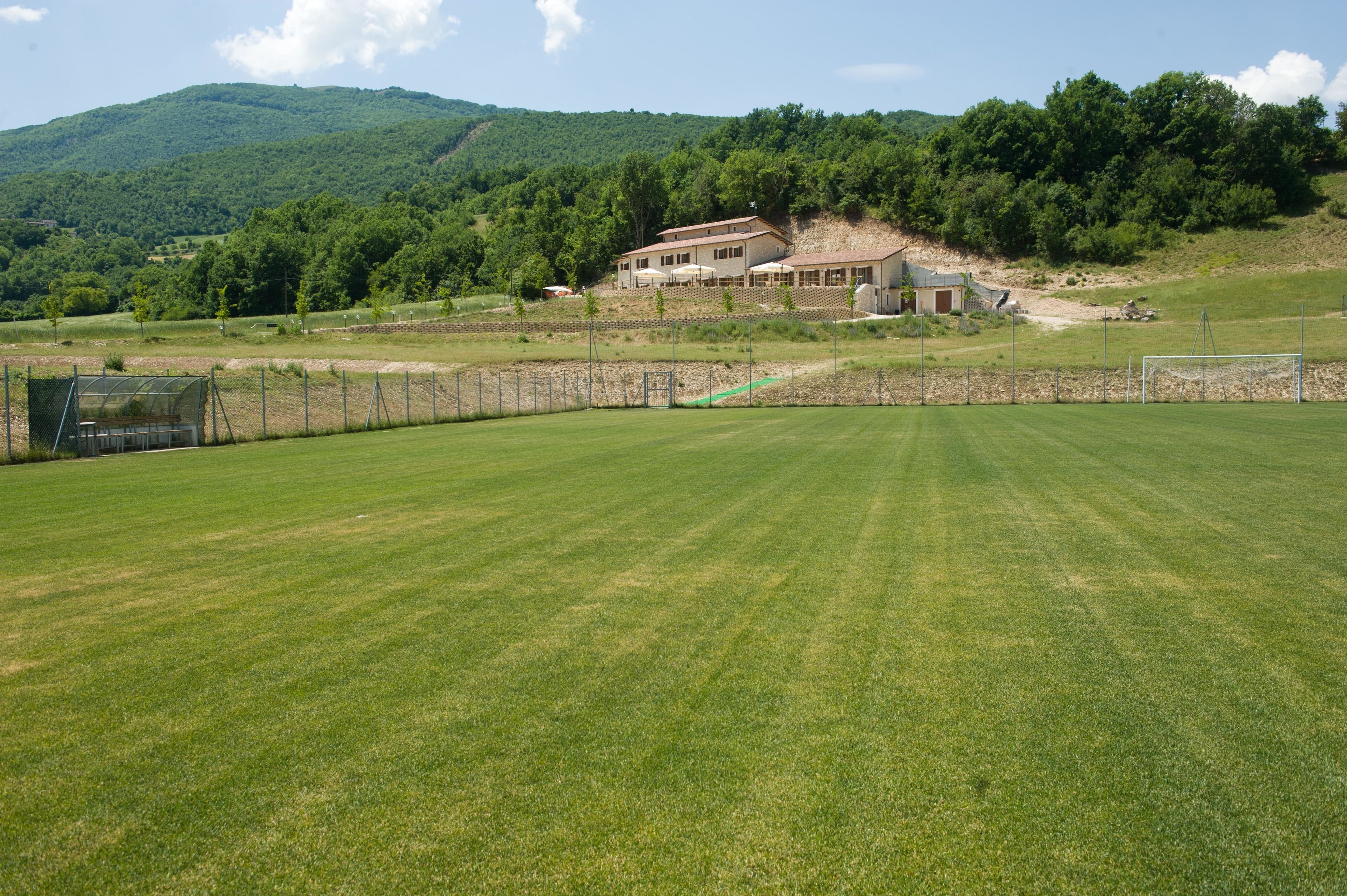 Un amplio campo cubierto de césped, bien cuidado, con una casa y una cancha de tenis al fondo.