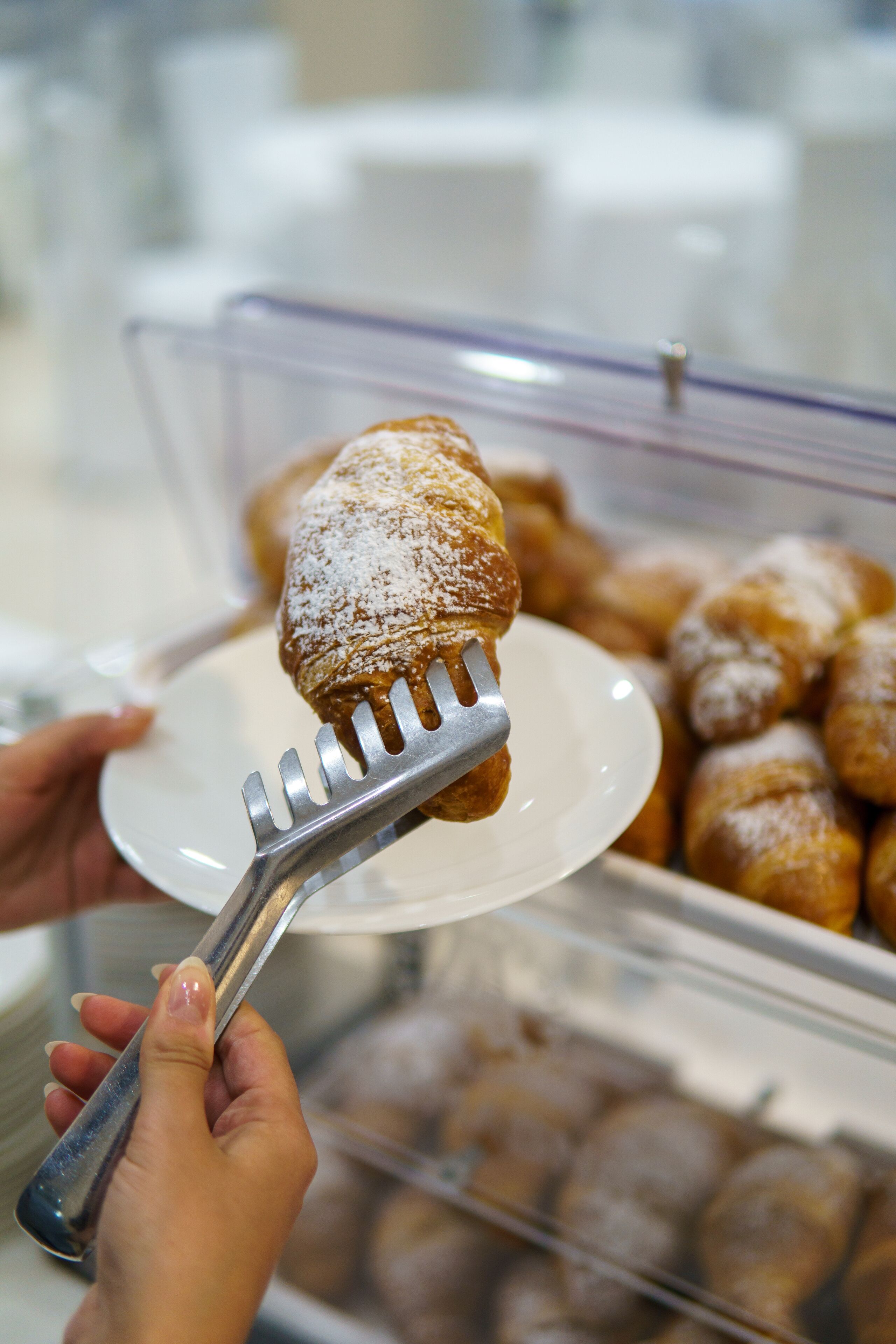 A hand holding a pastry with a fork, with more pastries in the background.