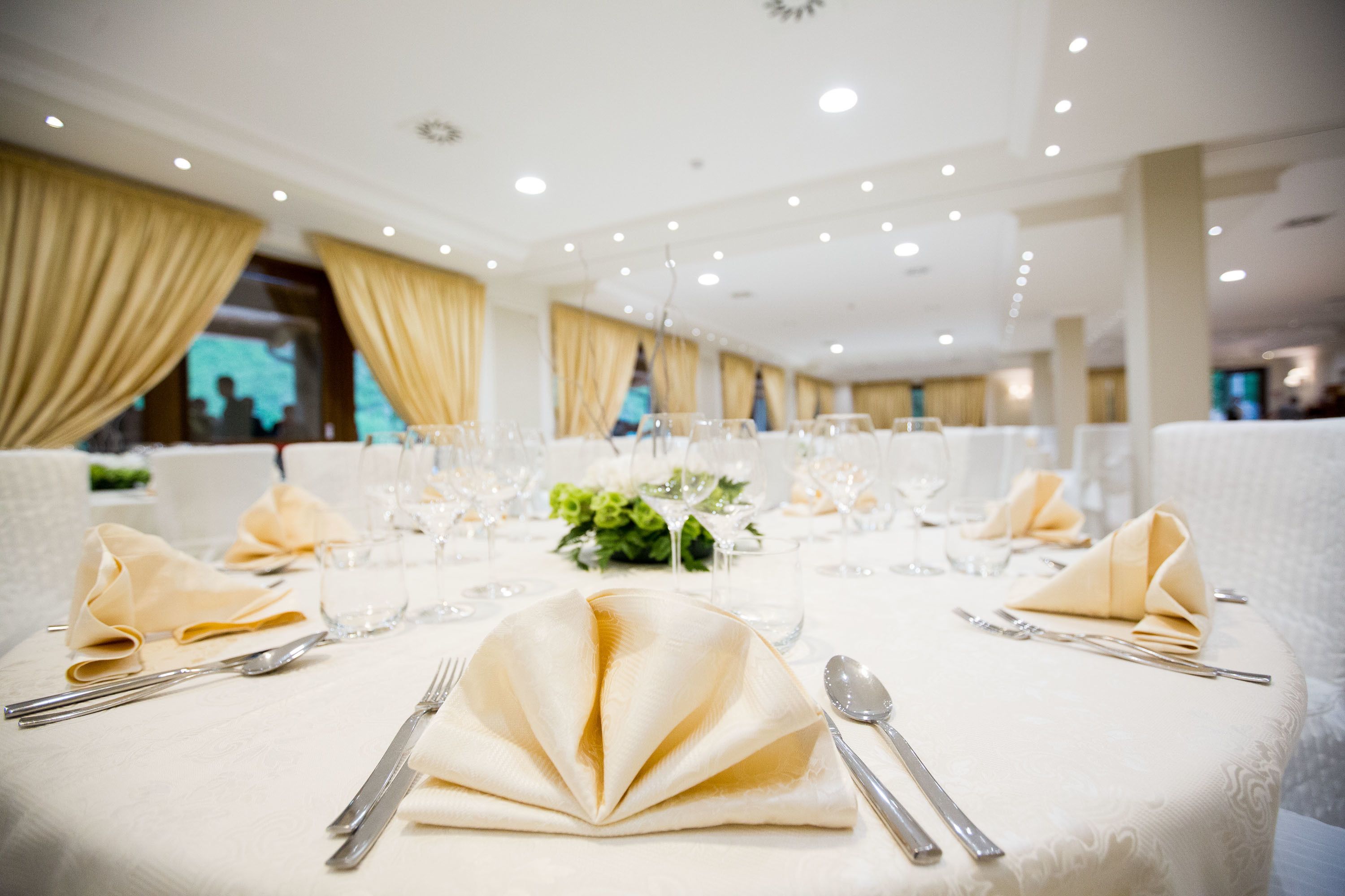Een feesttafel gedekt met witte tafellakens, gouden servetten en bestek.