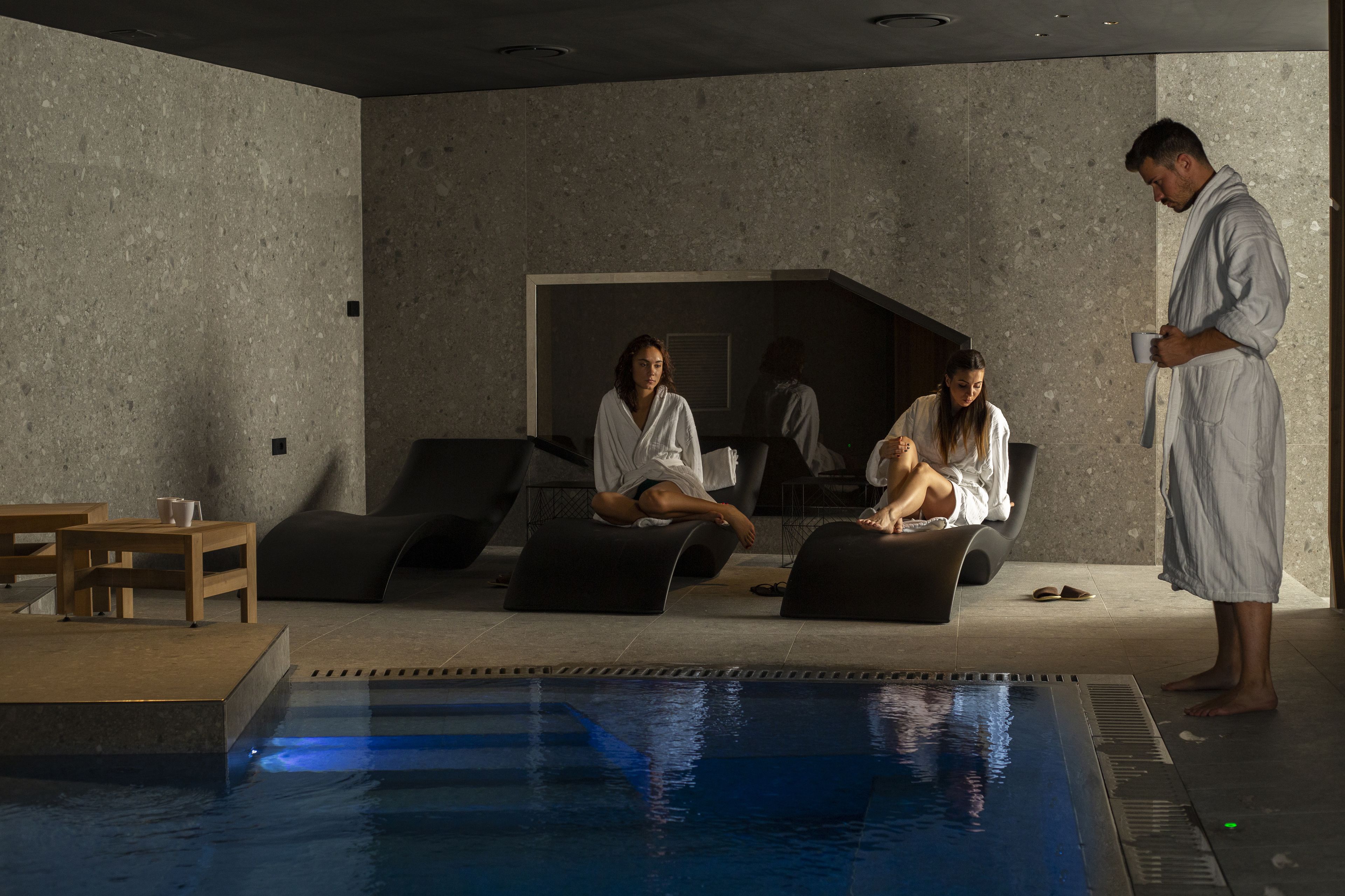 A modern indoor pool area with a lounge seating arrangement, a pool, and a person standing by the pool.