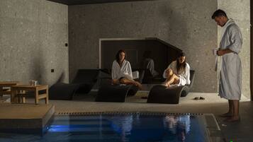 A modern indoor pool area with a lounge seating arrangement, a pool, and a person standing by the pool.