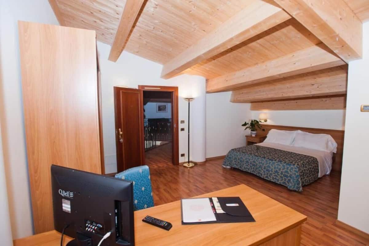A bedroom with a wooden ceiling, a bed with patterned bedding, a desk with a computer, and a bedside table.