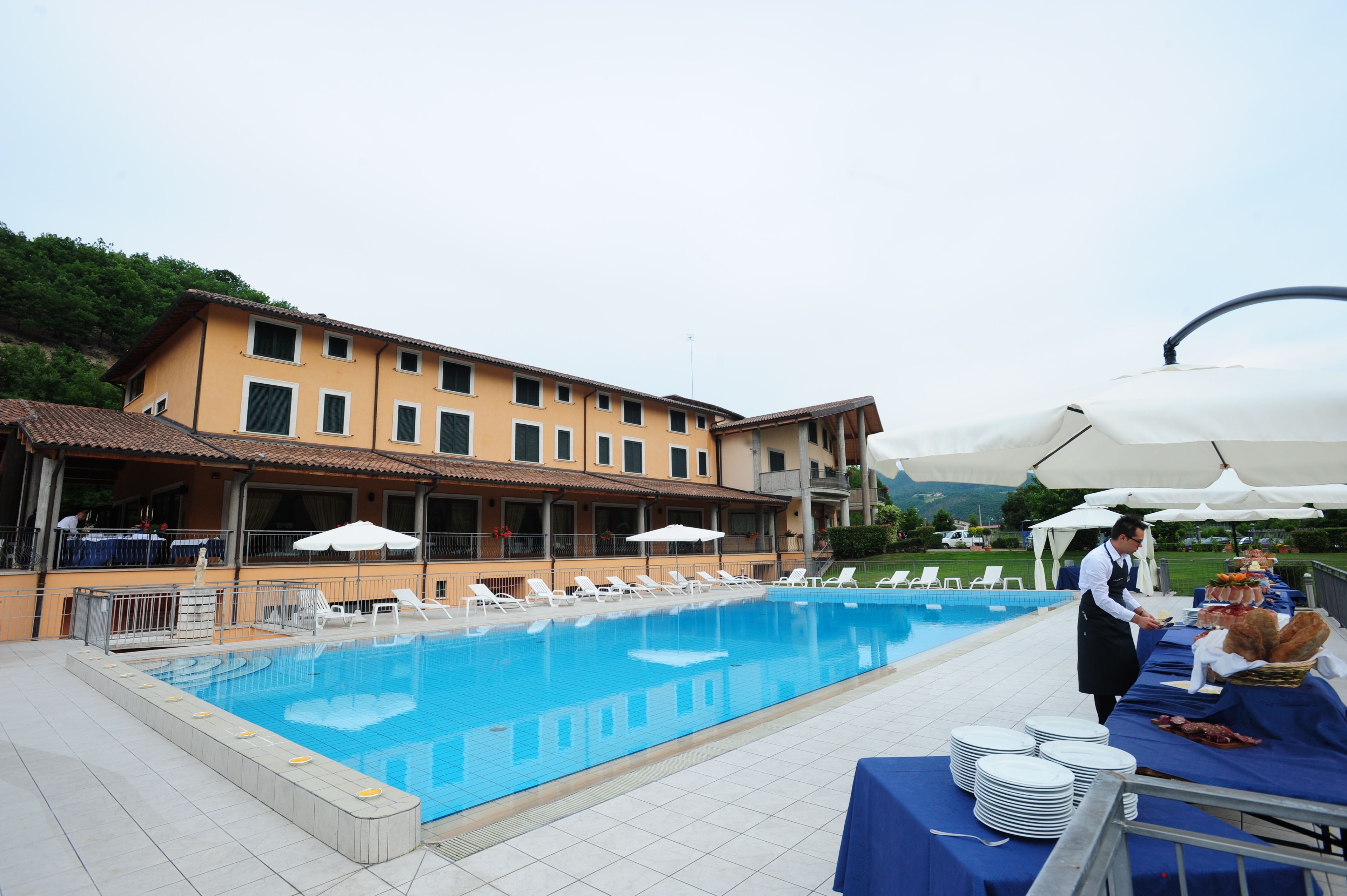 Une piscine avec des chaises longues, une table de buffet avec des assiettes, et un bâtiment doté de nombreuses fenêtres.