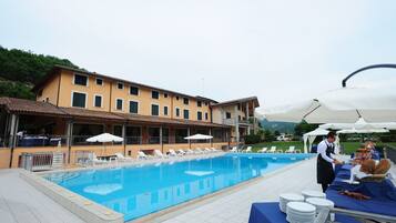 Une piscine avec des chaises longues, une table de buffet avec des assiettes, et un bâtiment doté de nombreuses fenêtres.