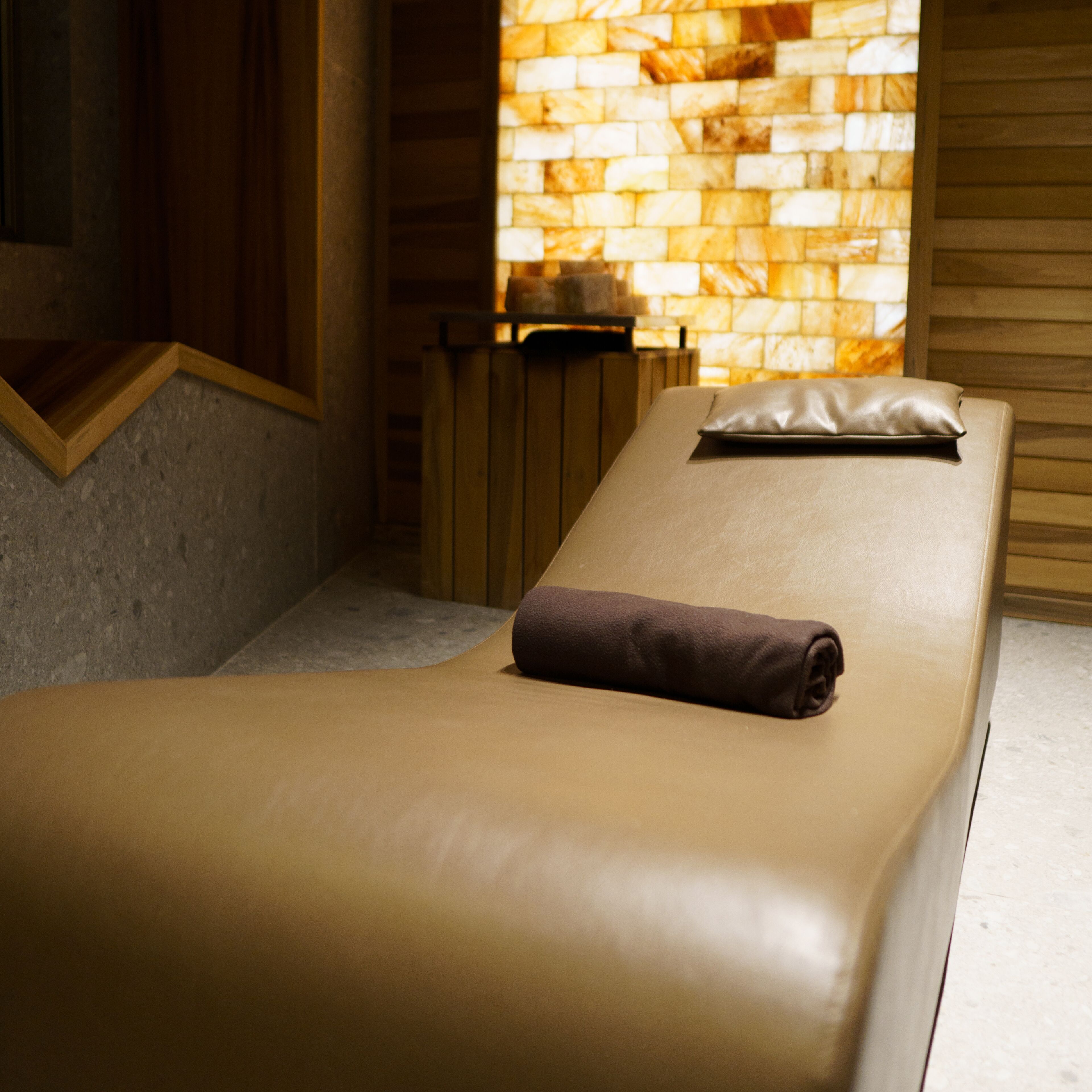 A spa room with a massage table, a wooden bench, and a stone wall with a window.