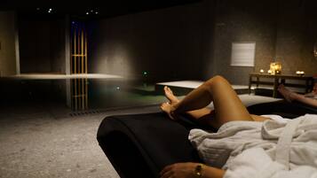 A person lying on a black lounge chair in a dimly lit room with a small table and candles.