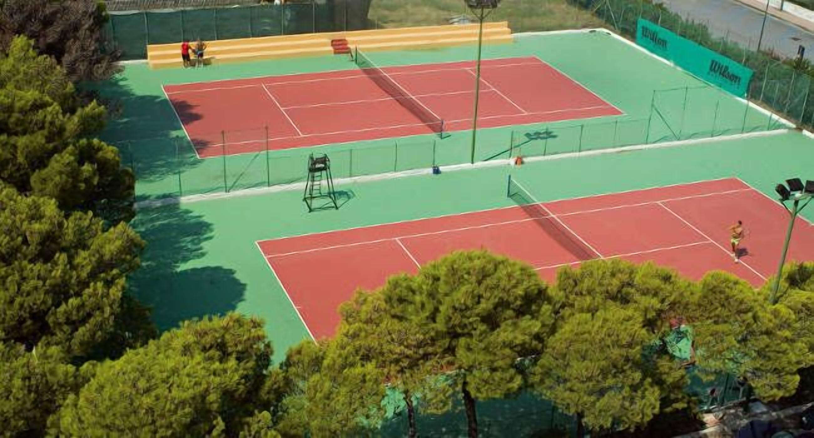 A tennis court with two courts, surrounded by trees and a fence.