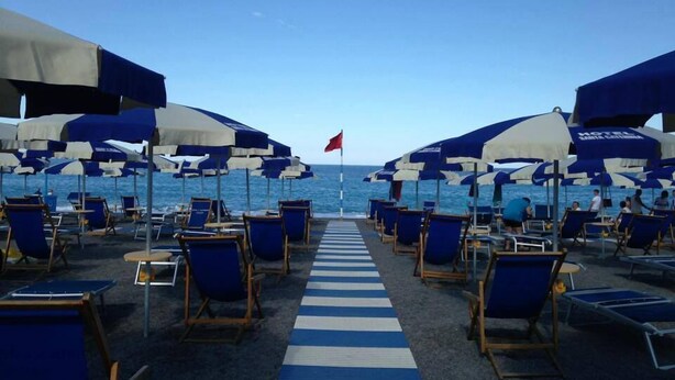A beachside hotel deck with rows of blue and white striped lounge chairs and umbrellas, leading to the ocean. - Hotel Village Club Santa Caterina (Scalea)