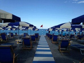A beachside hotel deck with rows of blue and white striped lounge chairs and umbrellas, leading to the ocean. - Hotel Village Club Santa Caterina (Scalea)
