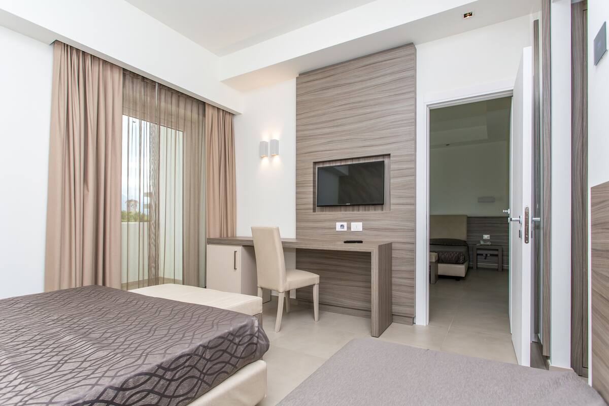 Ein modernes Hotelzimmer mit einem großen Bett, einem Schreibtisch, einem Sessel, einem Fernseher und einer separaten Wohnbereits mit einer Couch und einem kleinen Tisch.