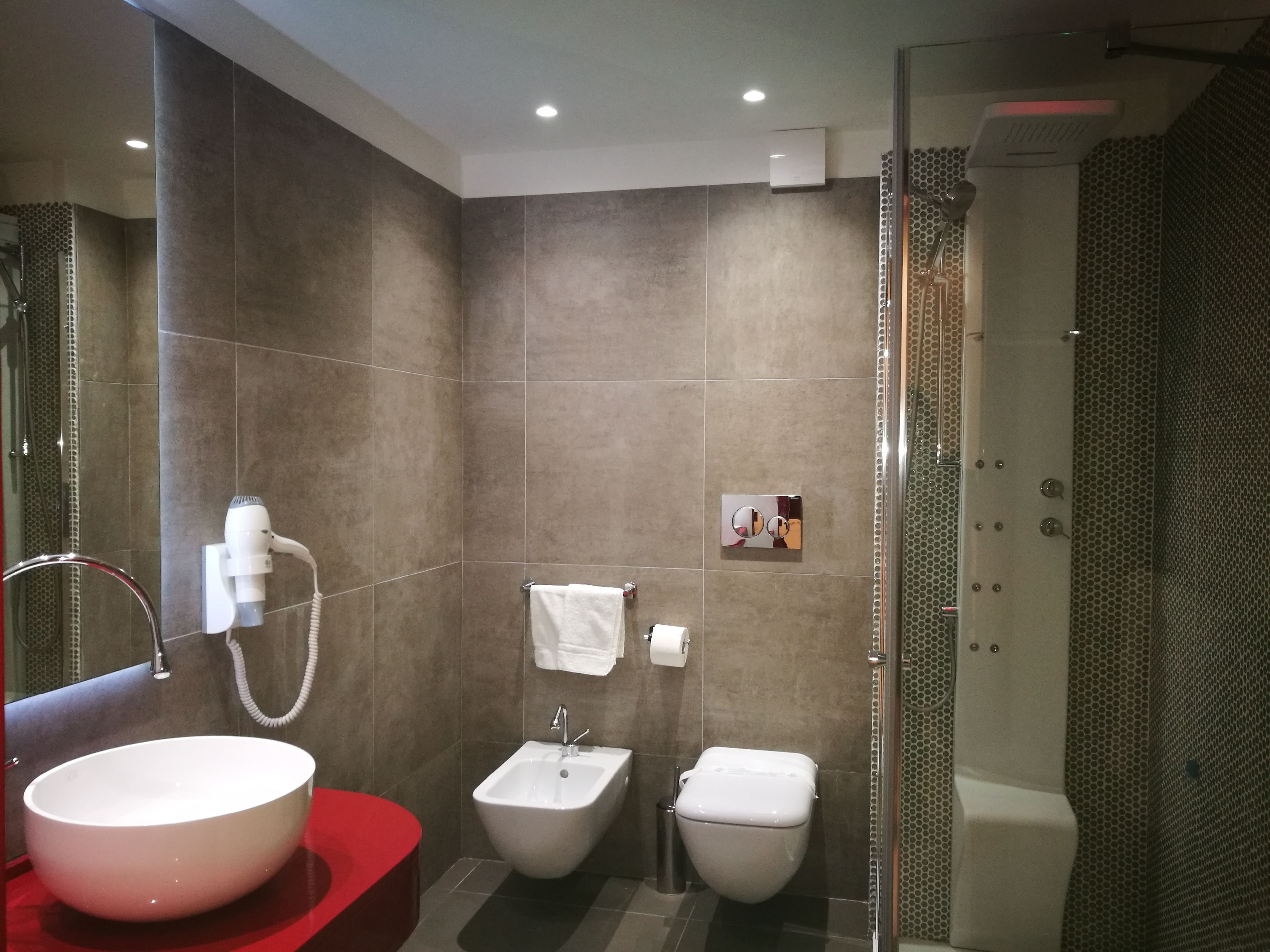 A modern bathroom with a large white sink, a red vanity, a bidet, and a shower enclosure.