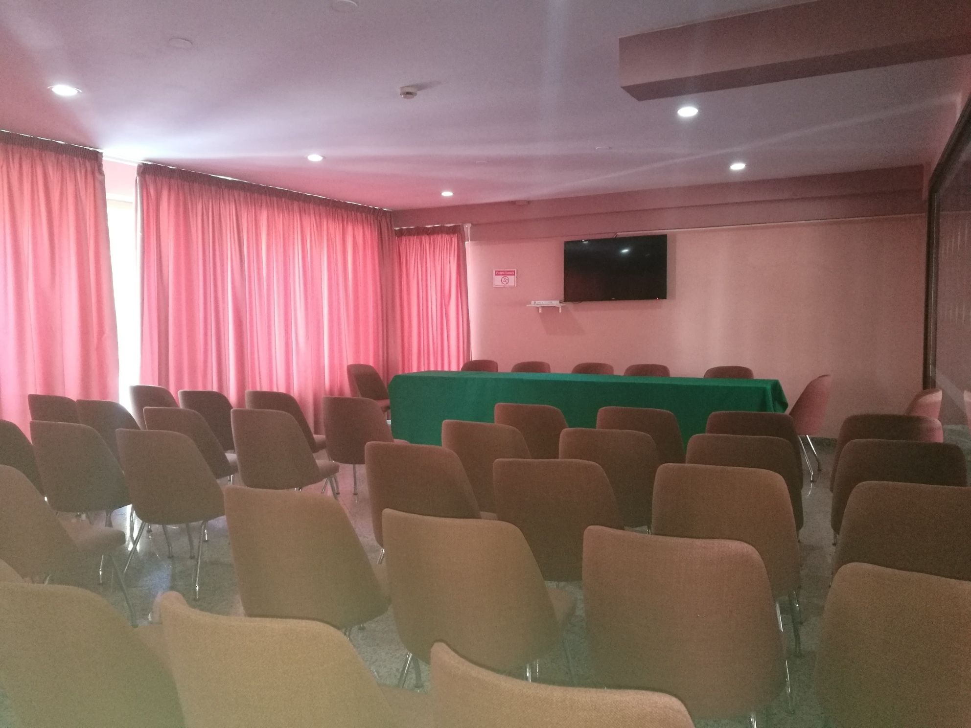 Ein Konferenzraum mit Reihen von Stühlen, einem grünen Tisch und einem Flachbildfernseher an der Wand.
