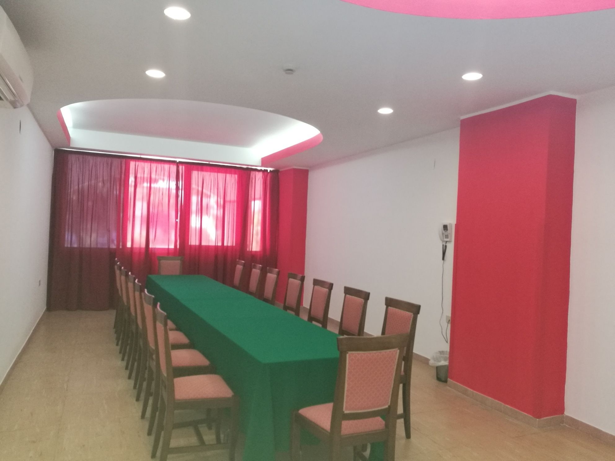 Une salle de conférence avec une longue table, des chaises, des rideaux rouges et un éclairage encastré au plafond.