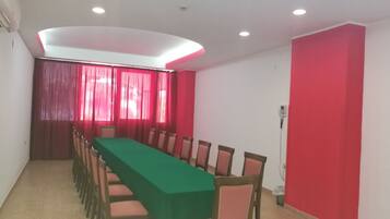 Une salle de conférence avec une longue table, des chaises, des rideaux rouges et un éclairage encastré au plafond.