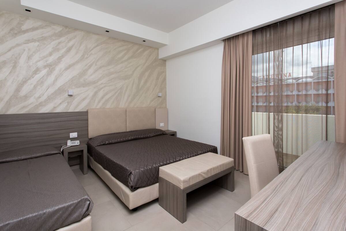 Ein modernes Hotelzimmer mit einem großen Bett, einem kleineren Bett, einem Schreibtisch und einem Sessel.