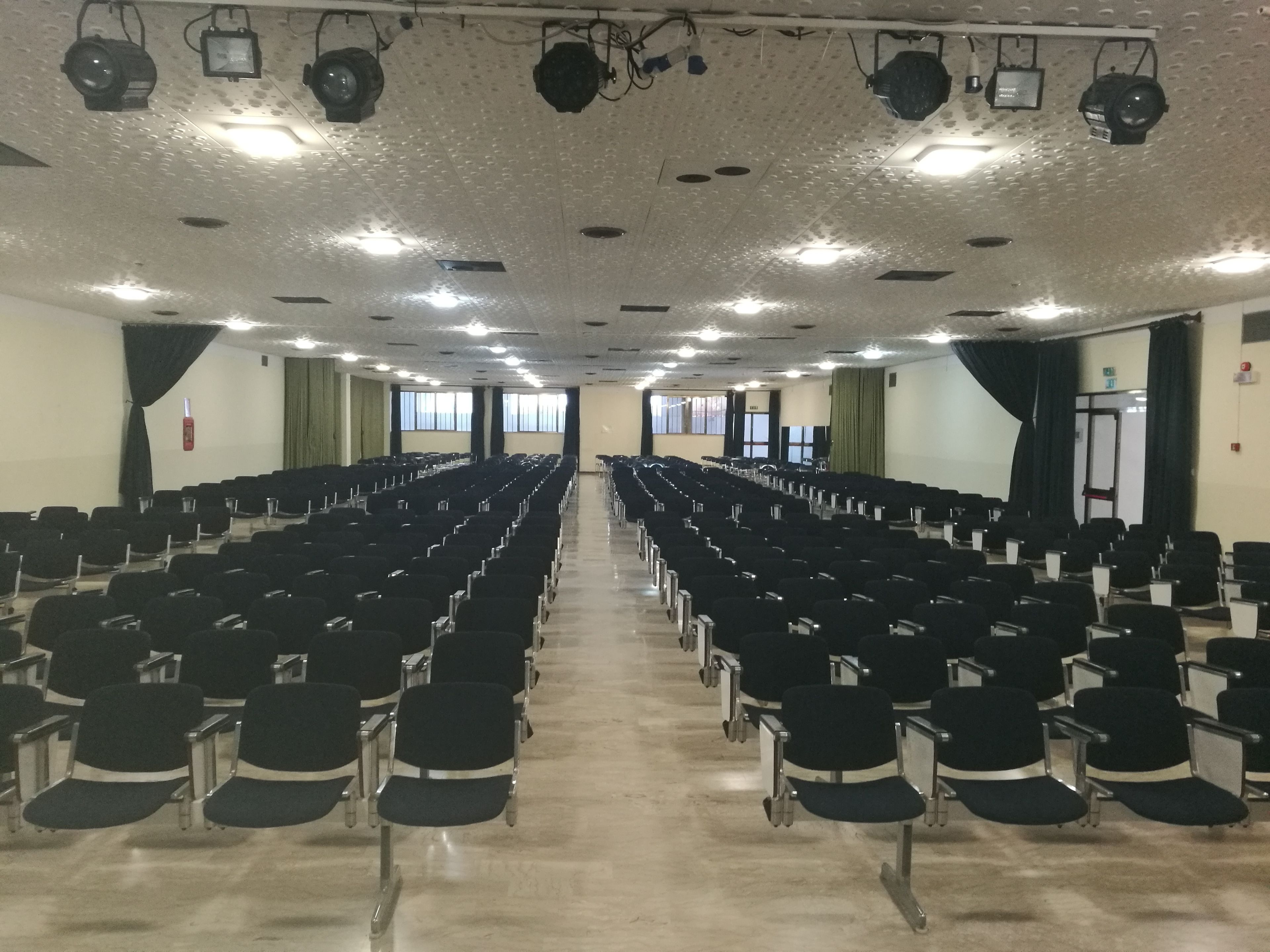 A conference room with rows of chairs, ceiling lights, and windows.