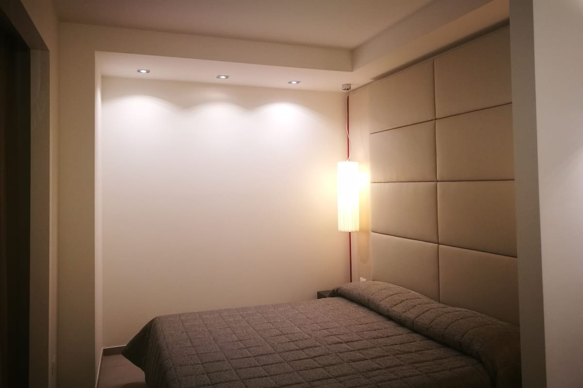 Ein Schlafzimmer mit einem Bett, einem Nachttisch und einer wandmontierten Lampe.