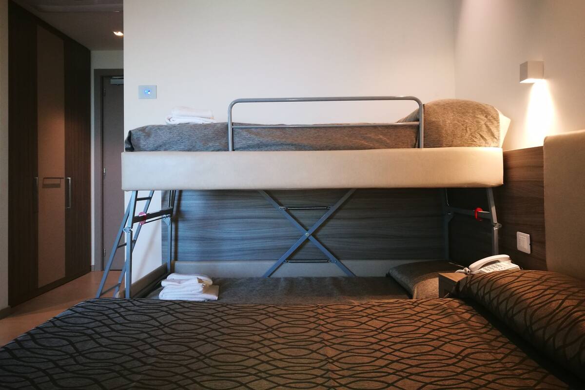 Ein Stockbett mit Schreibtisch und Telefon, eine gestreifte Bettdecke und eine Wandleuchte.