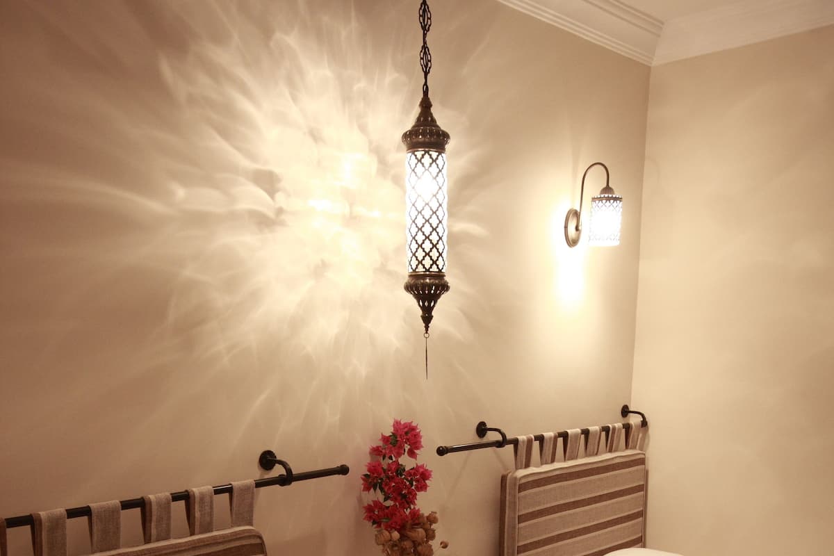 A hotel room with two beds, a nightstand, a vase with flowers, and a wall-mounted light fixture.