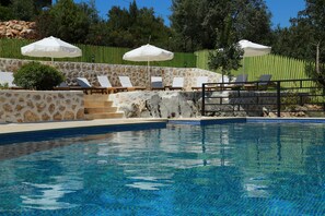 A swimming pool with lounge chairs and umbrellas, surrounded by stone walls and a green fence. - Dardanos Hotel (Kas)
