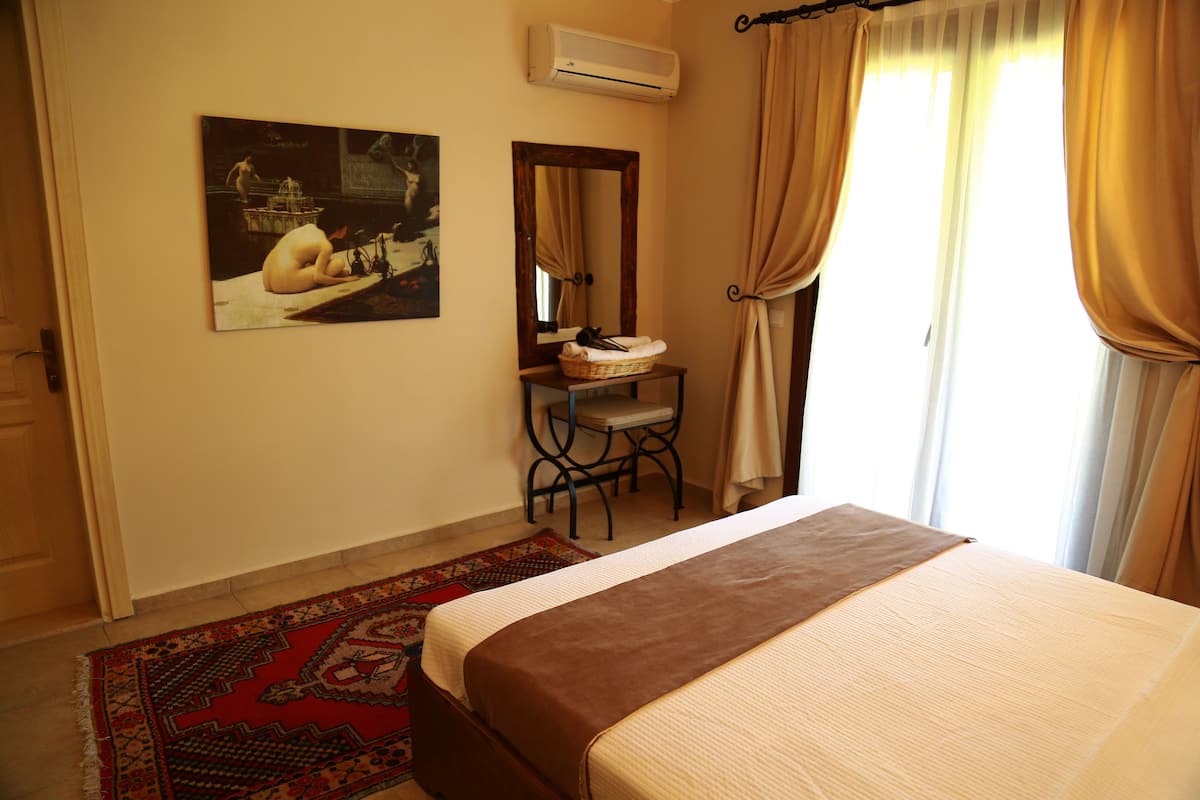 A bedroom with a bed, a desk with a chair, a mirror, and a painting on the wall.