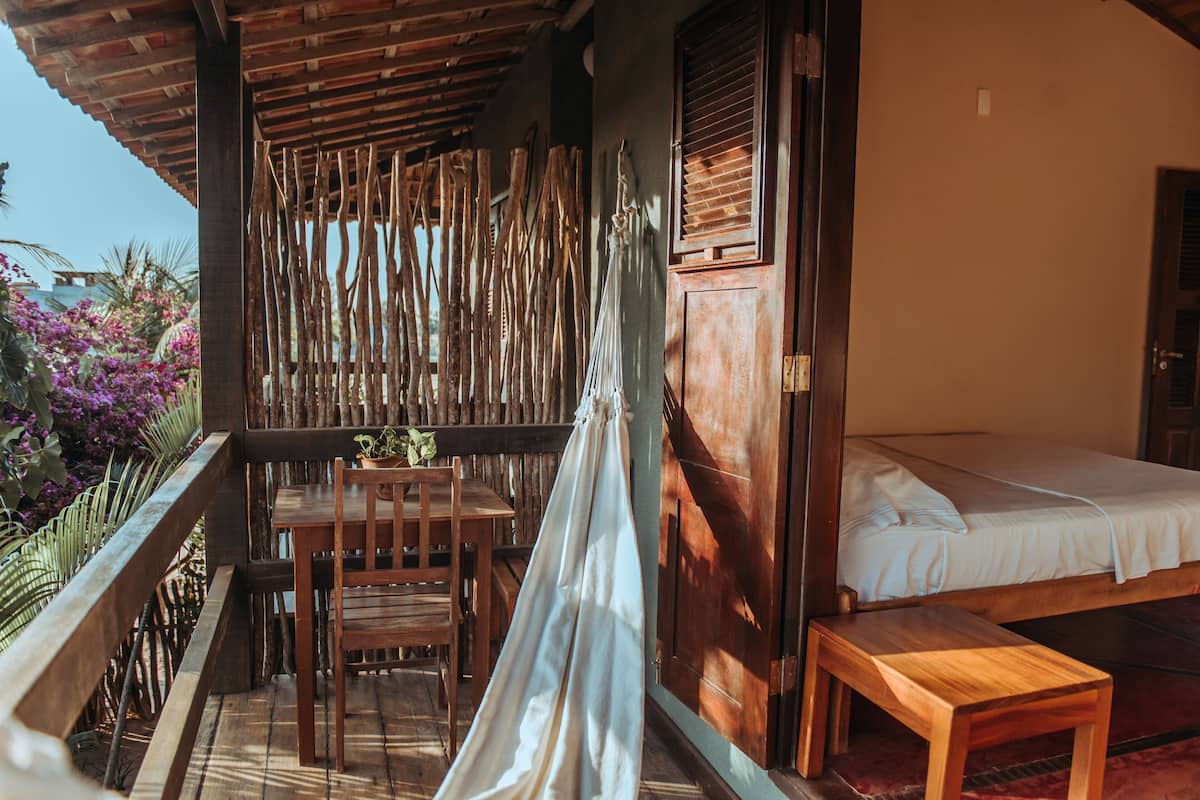 Varanda de madeira com mesa, cadeiras, cama e rede.