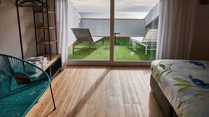 A room with a bed, a green chair, a small table, a balcony with two chairs, and a metal rack with hangers. - Hotel Vila de Premià (Premia de Mar)
