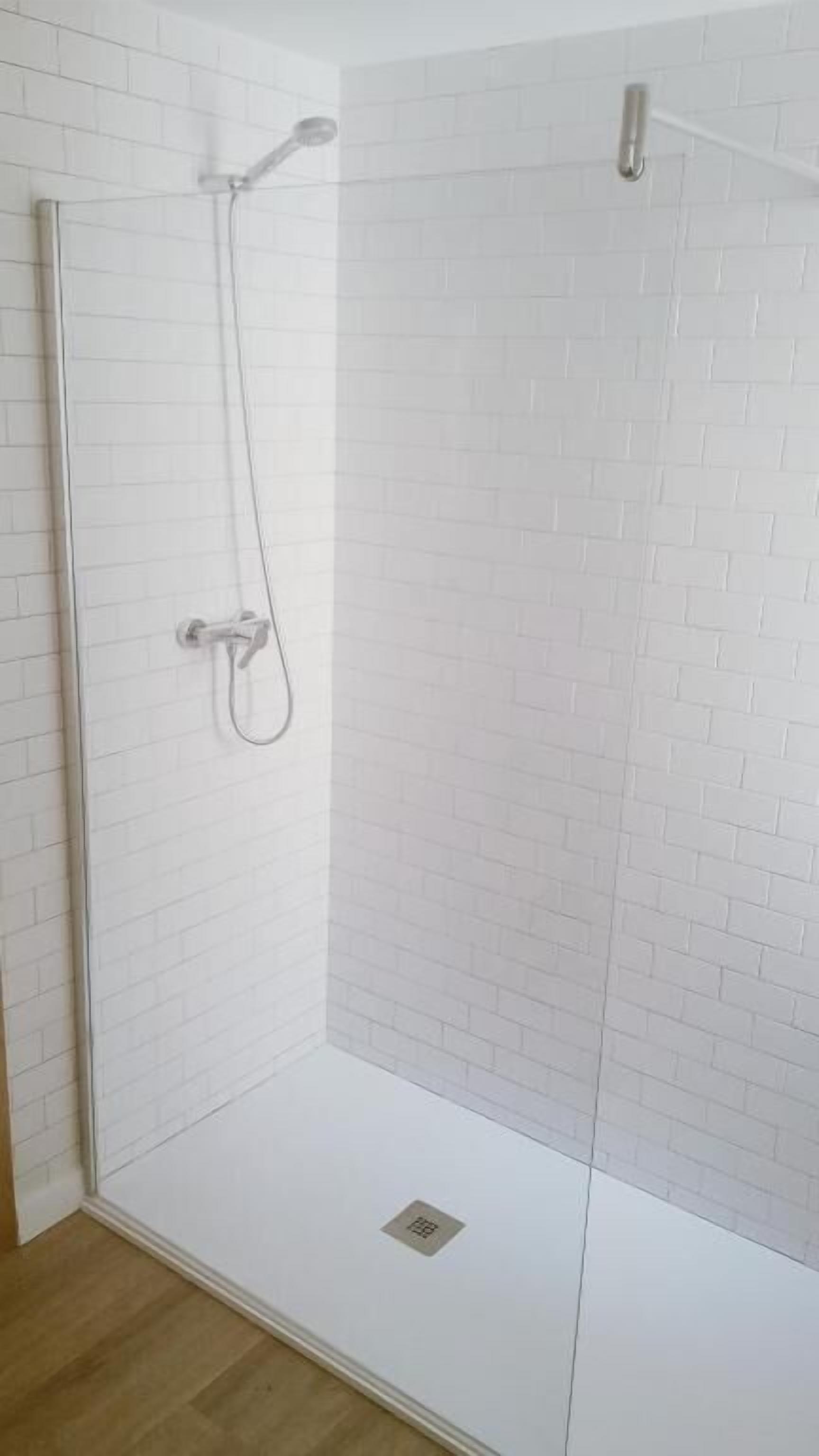 A glass-enclosed shower with a white brick wall and a wooden floor.