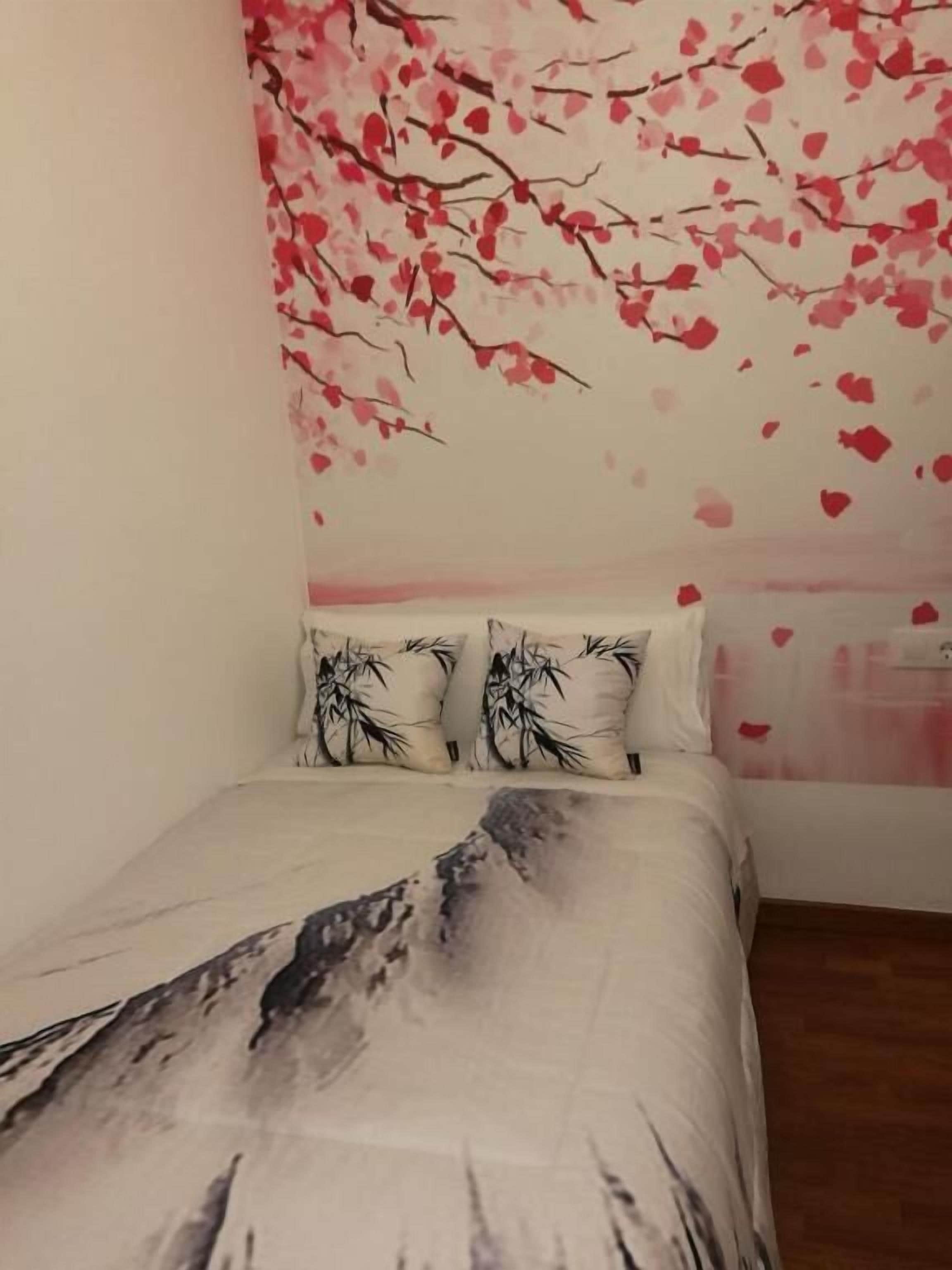 Un dormitorio con una cama, dos almohadas con diseños de bambú y una pared decorada con motivos de cerezos en flor.