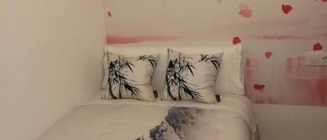 Un dormitorio con una cama, dos almohadas con diseños de bambú y una pared decorada con motivos de cerezos en flor.