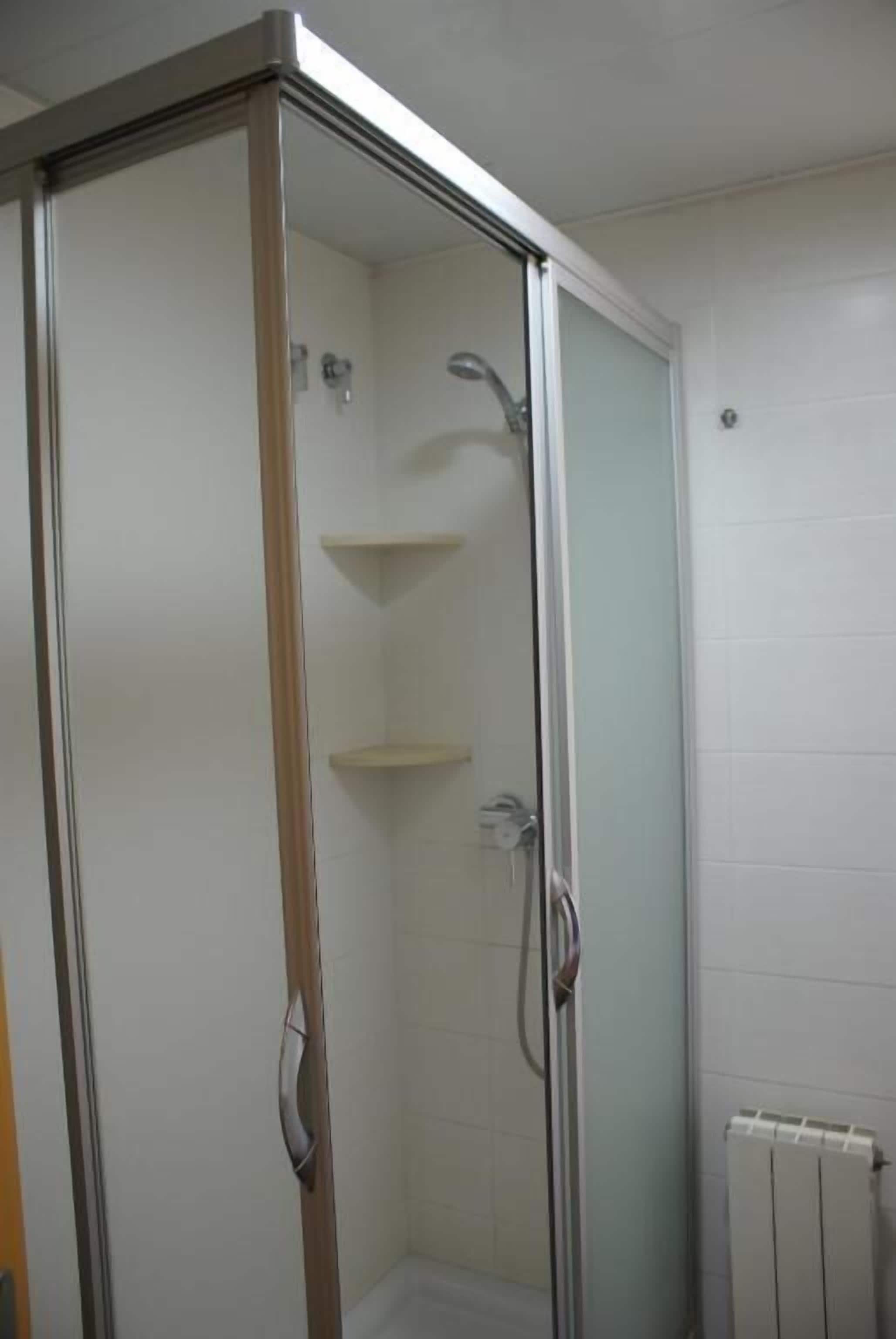 Mampara de ducha con puerta de cristal, marco metálico y pared de azulejos blancos.