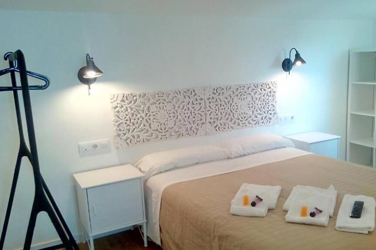 A hotel room with a bed, bedside lamps, a white headboard, a nightstand, a wardrobe, and a shelf.
