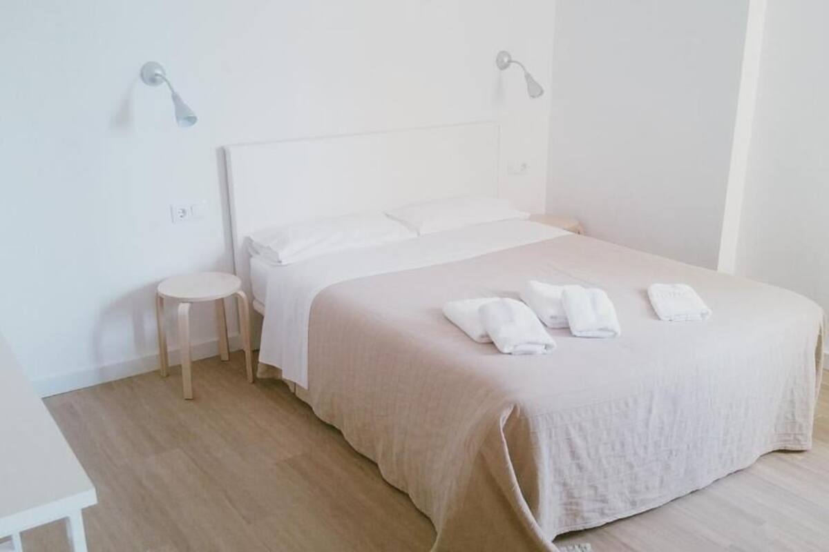 A minimalist bedroom with a bed, bedside tables, and wall-mounted lights.