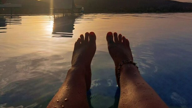 Una persona relajándose en una piscina infinita con un atardecer de fondo.