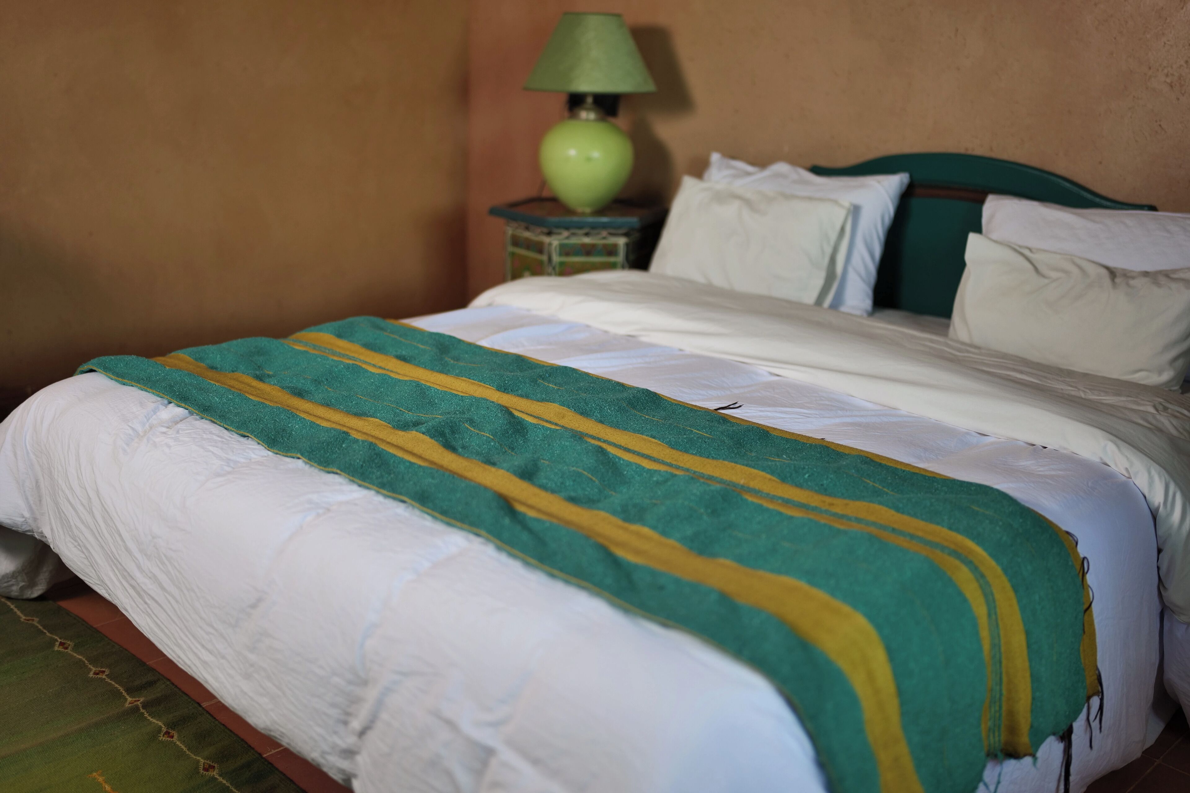 A bed with a green and yellow striped blanket, a green headboard, and white pillows.