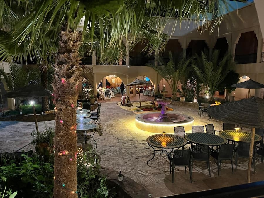 An outdoor patio area with tables and chairs, a central fountain, and palm trees.