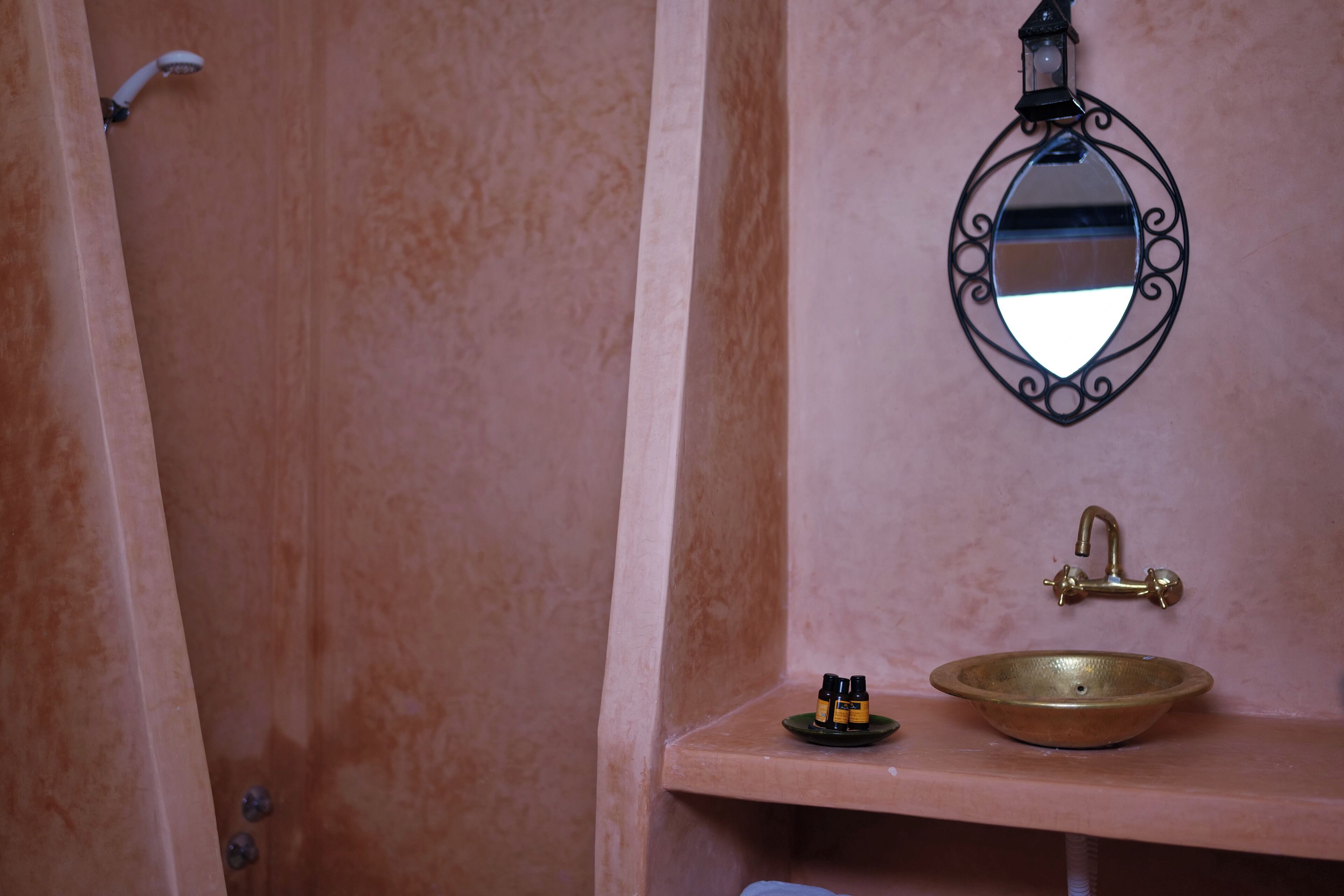 Une salle de bain avec un lavabo, un miroir et une petite étagère sur laquelle sont posées des bouteilles.