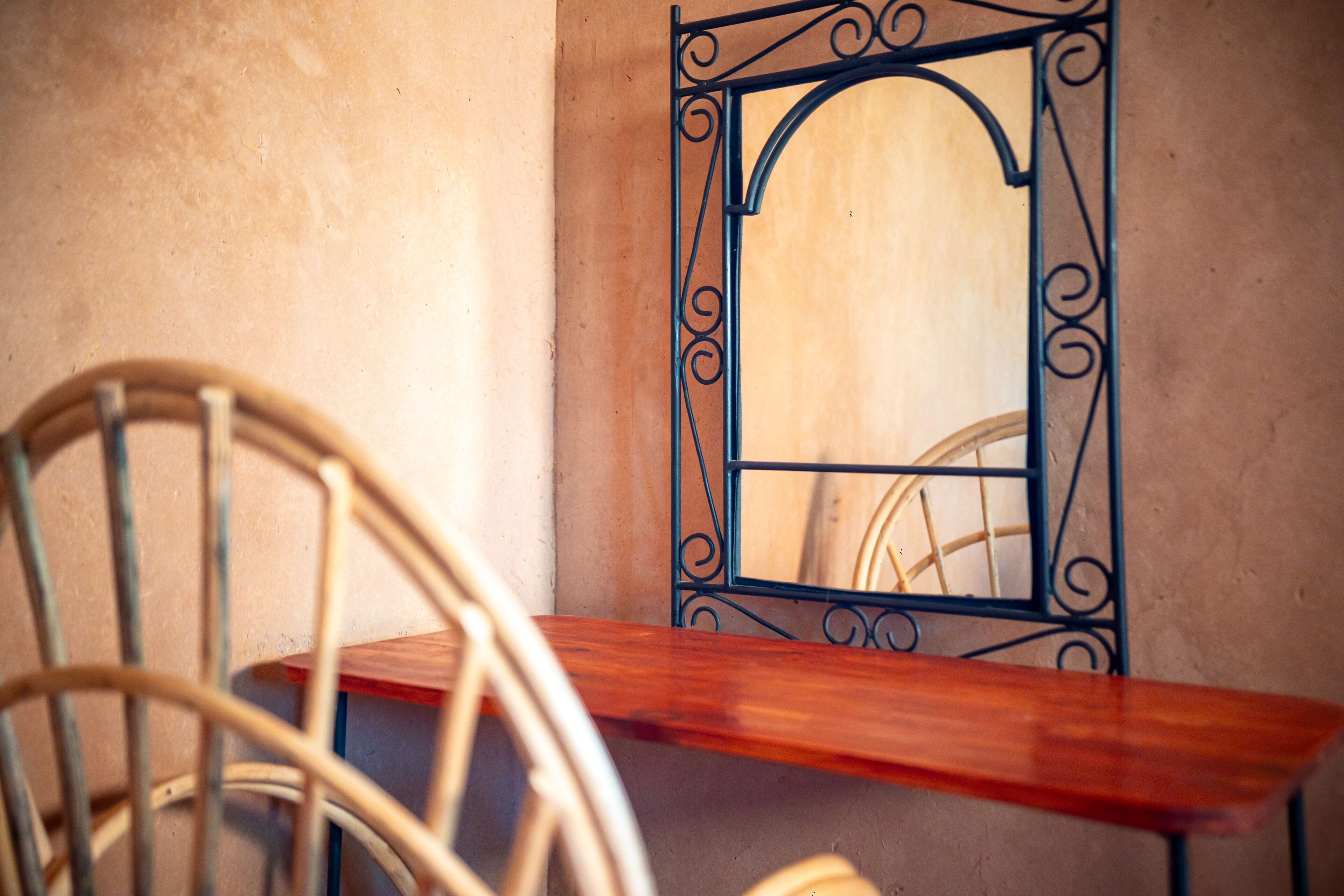 Una silla y una mesa de madera con un marco metálico decorativo frente a una pared con textura.