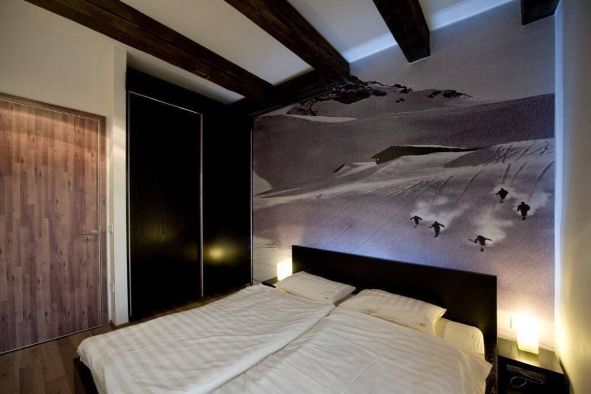 Une chambre dotée d’un grand lit, de poutres apparentes en bois au plafond, d’une fresque murale représentant un paysage enneigé et d’une armoire.