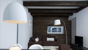 Un salon moderne avec un plafond en bois foncé, un canapé marron avec des coussins blancs, un meuble TV noir et un grand lampadaire blanc.