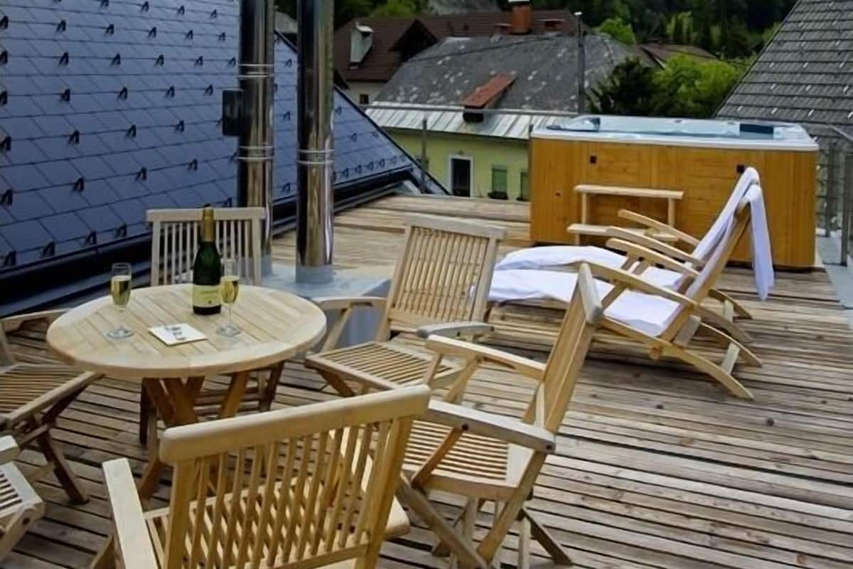Une terrasse en bois avec coin salon extérieur et jacuzzi, offrant une vue sur un paysage montagneux.