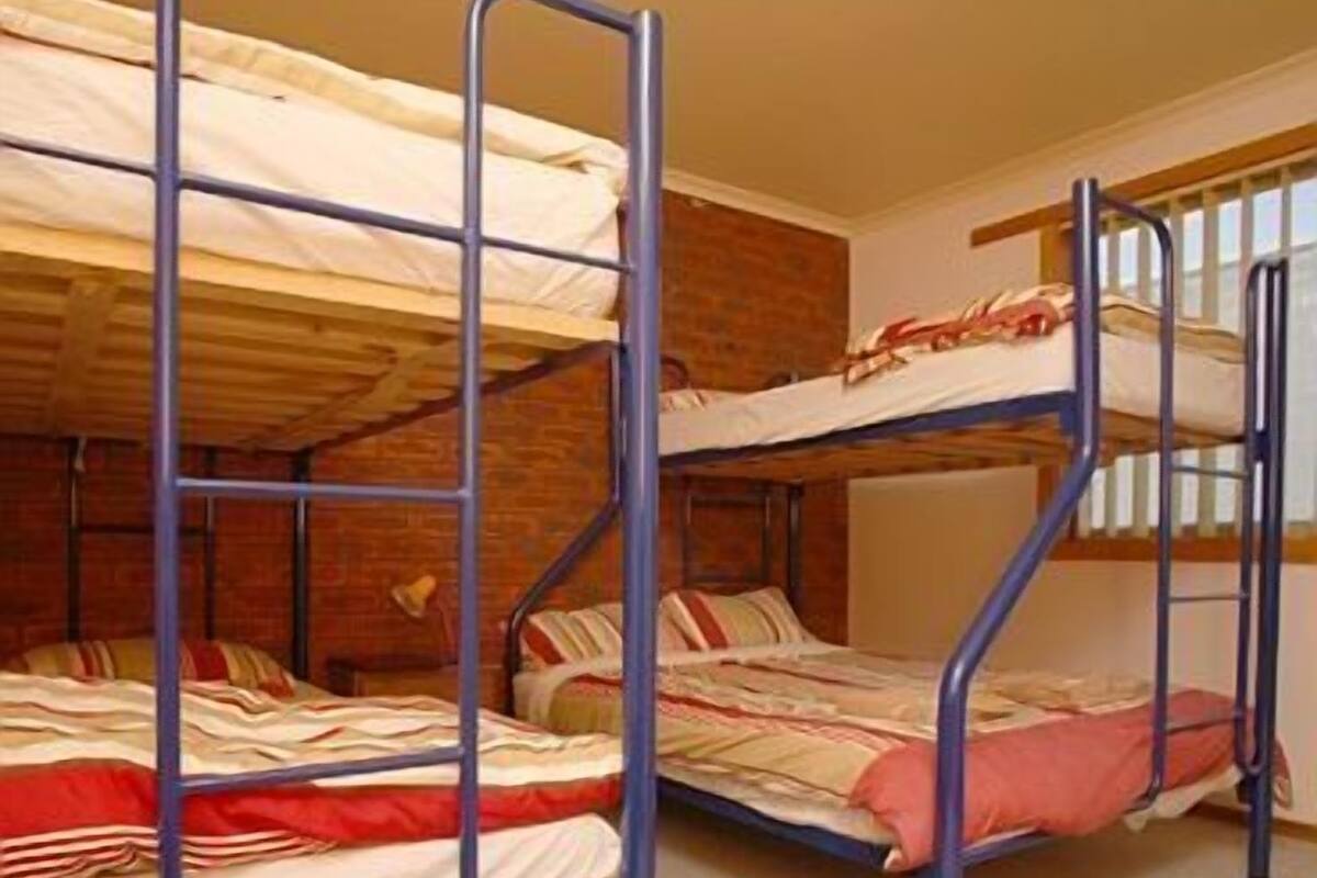 Quarto de dormitório com beliches, uma escrivaninha de madeira e parede de tijolos.