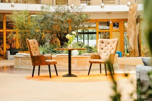 A lobby with two leather armchairs, a round table, and a large plant in the center. - Rabenstein (Raben Steinfeld)