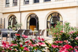 An outdoor seating area with tables and chairs, surrounded by a building with arched windows and a brick facade. - Rabenstein (Raben Steinfeld)