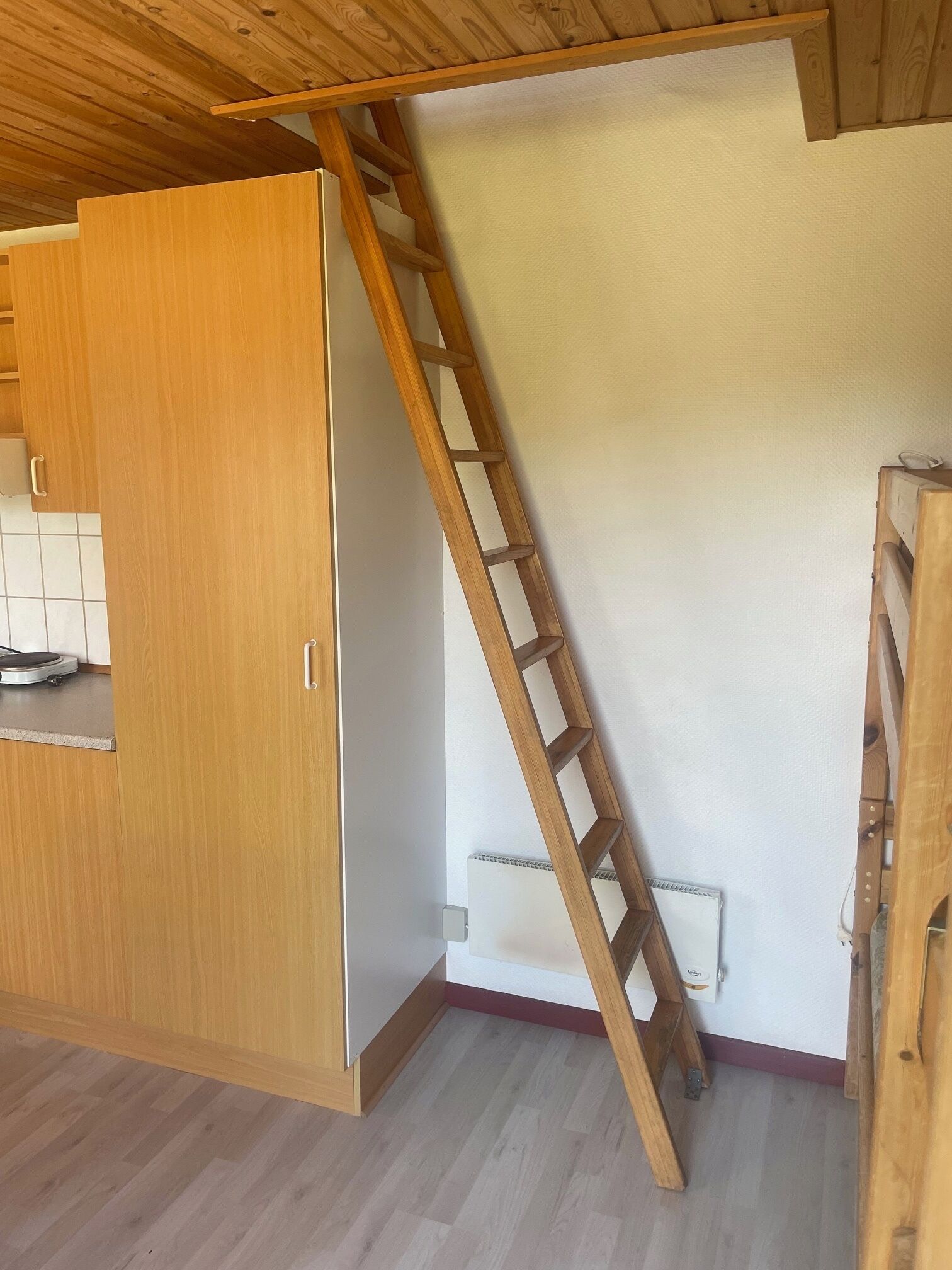Una habitación con un armario de madera, una escalera de madera y una pared blanca.