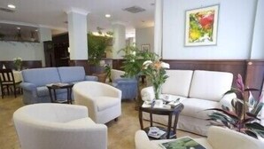 Un vestíbulo de hotel con una zona de estar que incluye sofás y sillones, una mesa de centro y plantas en macetas.