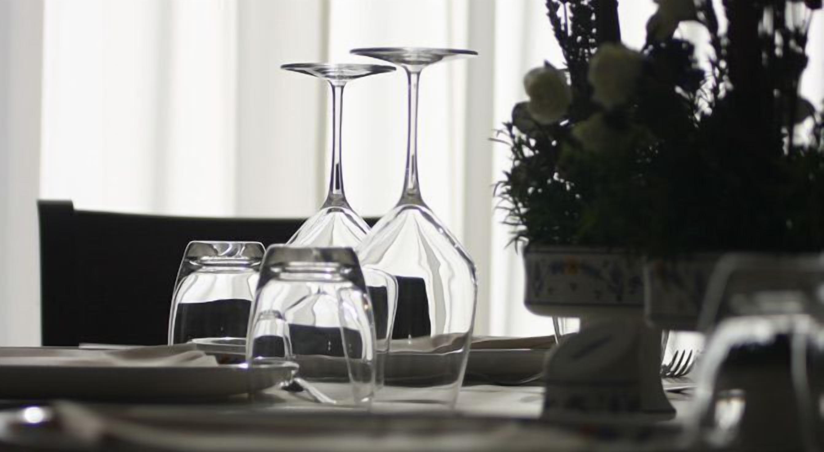 Et spisebord med blanke glas og tallerkener, en vase med blomster og et vindue i baggrunden.