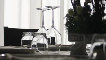 Et spisebord med blanke glas og tallerkener, en vase med blomster og et vindue i baggrunden.
